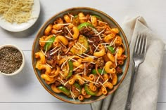 a bowl filled with pasta and meat on top of a table next to a fork