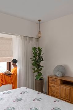 a woman in an orange robe is sitting on a bed looking out the window at the ocean