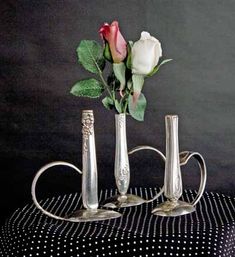 three silver vases with roses in them sitting on a black and white table cloth