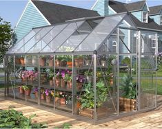 a greenhouse with potted plants and flowers in front of a blue house on a wooden deck