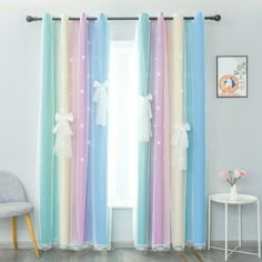 colorful curtains with white bows are hanging in front of a window, next to a chair