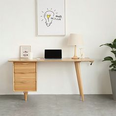 a wooden desk with a laptop on it next to a potted plant and lamp