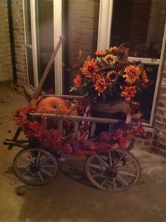 a wheelbarrow with flowers and pumpkins on the front porch at night time