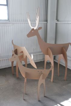 three cardboard deer standing next to each other in front of a white wall and window