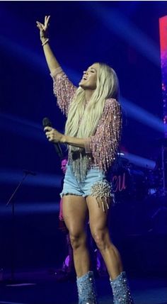 a woman in short shorts and boots on stage with her hand up to the sky