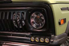 the front end of a green jeep with its lights on