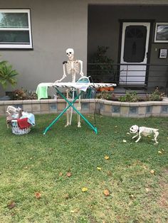 a skeleton sitting on top of a lawn next to a table with two skeletons in it