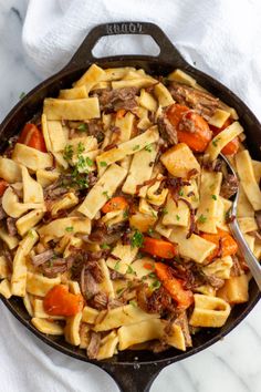 a skillet filled with pasta and meat on top of a white towel next to a fork