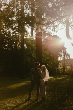 a bride and groom are standing in the grass near some trees at their wedding day