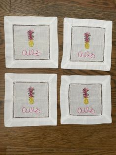 four embroidered pineapple napkins on top of a wooden table