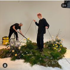 two people in black shirts are doing flower arrangements with hoses and flowers on the ground