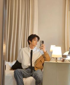 a person sitting on a bed with a cell phone in his hand and a lamp next to him