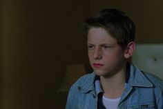 a young boy in a denim jacket stares into the distance