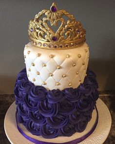 a three tiered cake decorated with purple and white icing, topped with a gold crown