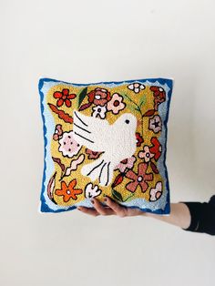 a person holding up a decorative pillow with a bird on the front and flowers on the back