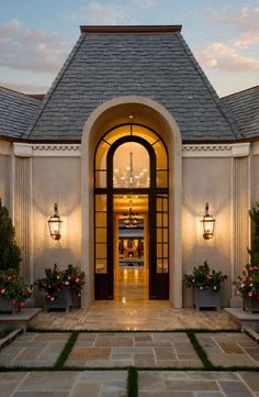 the front entrance to a large home with potted plants and lights on either side