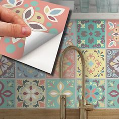 a hand holding a piece of paper over a sink with colorful tiles on the wall behind it