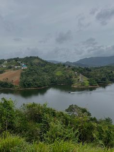 a large body of water surrounded by lush green trees and hills in the distance with houses on top