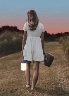 a woman is walking in the grass with a light on her head and a suitcase