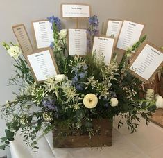 a wooden box filled with lots of flowers on top of a white cloth covered table