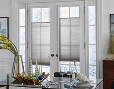 a glass table topped with vases filled with flowers next to two windows covered in blinds