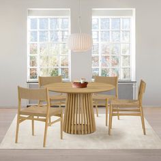 a round table with four chairs around it in front of two windows and a rug on the floor