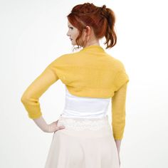 a woman with red hair wearing a yellow cardigan and white skirt, back view