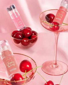 two martini glasses filled with cherries next to a bottle of cherry water and a bowl of cherries