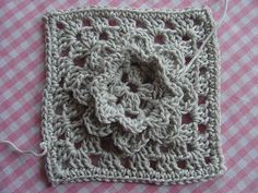 there is a crocheted square with a flower in the center on a pink and white checkered tablecloth