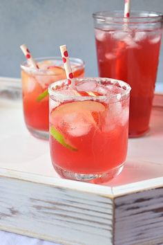 two glasses filled with red drinks sitting on top of a wooden tray next to each other