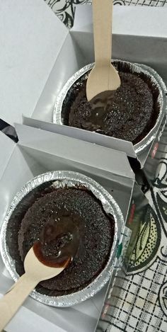 two pies in boxes with spoons sticking out of the top and one has chocolate frosting on it