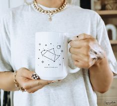 a woman holding a coffee mug with the zodiac sign sagith on it's side