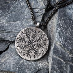 a pendant with an intricate design on it is sitting on some rocks and has a chain attached to it