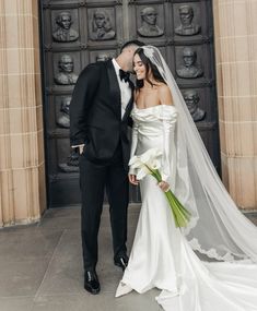 a bride and groom standing in front of an ornate door with the veil blowing in the wind