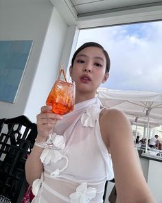 a woman holding a wine glass in her right hand and wearing a white dress with flowers on it