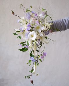 a bouquet of white and purple flowers is being held by someone's hand in front of a wall