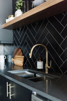 a black kitchen with gold faucet and stainless steel sink, shelving above the counter