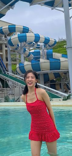 a woman in a red dress standing next to a pool with water slides behind her