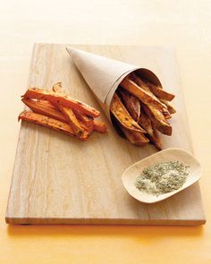 a wooden cutting board topped with french fries next to a small bowl of dipping sauce