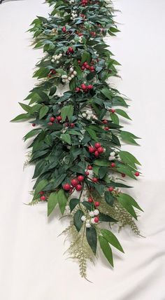 a long row of green leaves and red berries with white flowers on the top one