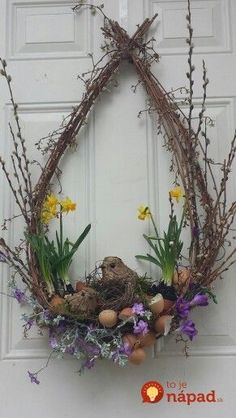 a wreath with flowers, eggs and twigs hanging on the front door for easter decoration