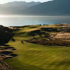 an aerial view of a golf course near the water with mountains in the back ground