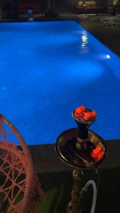 an empty swimming pool at night next to a chair and table with food on it