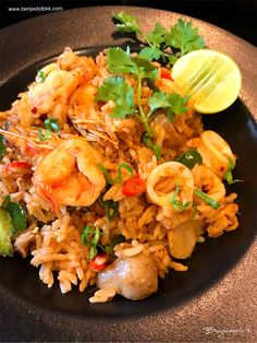 a black plate topped with rice and shrimp next to a lemon wedge on top of a table