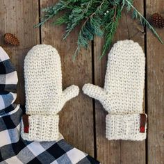 a pair of white knitted mittens sitting on top of a wooden floor next to a pine tree