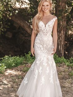 a woman in a wedding dress posing for the camera with trees in the back ground