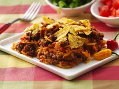 a white plate topped with taco salad next to a bowl of tomatoes and tortilla chips