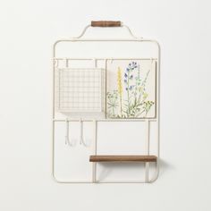 a white wall mounted shelf with two hooks and flowers on the top, hanging from it's side