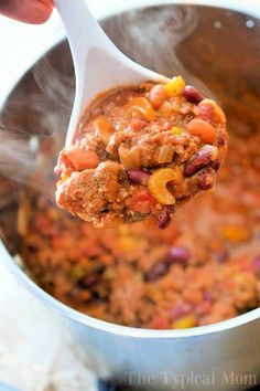 a ladle full of chili and beans being stirred with a spoon