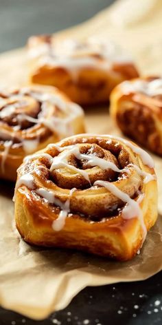 cinnamon rolls with icing sitting on top of a piece of parchment paper next to each other